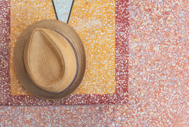 Overhead view of Trilby straw hat laying on top of Mediterranean style Terrazzo stone bench and floor - Aerial shot of a mens hat on  stylish summer alfresco outdoor patio - Trendy and fashion concept