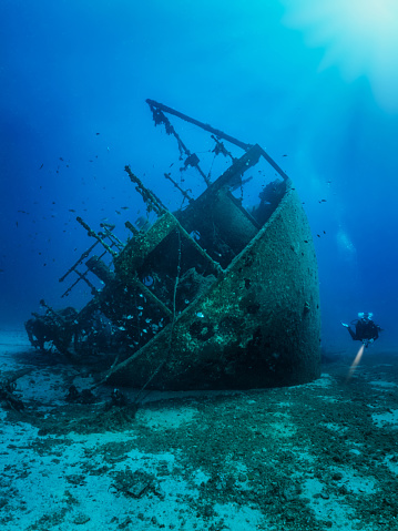 An old, sunken wreck on the seabed of the Aegean Sea in Greece with a unrecognizable scuba diver exploring it
