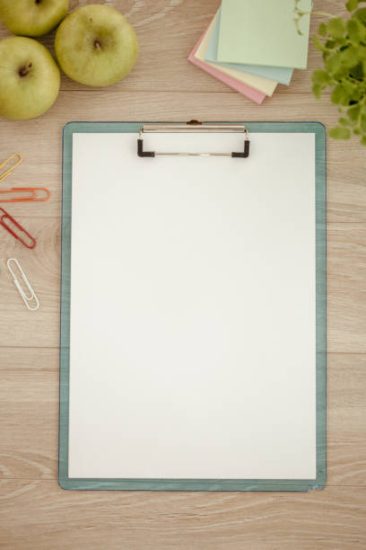 Clipboard with blank paper, adhesive notes office supplies and apples at office desk.