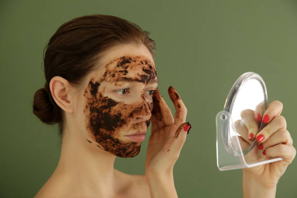 istock Woman applying coffee scrub in front of the mirror, studio shot. 1175868733