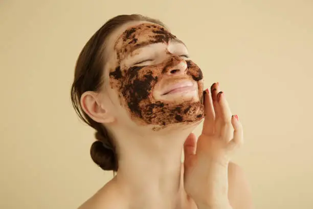 Photo of Woman exfoliating face with a coffee scrub, studio shot.