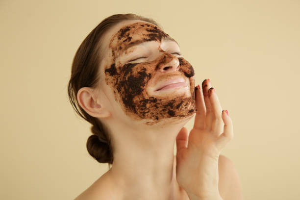 woman exfoliating face with a coffee scrub, studio shot. - face mask imagens e fotografias de stock