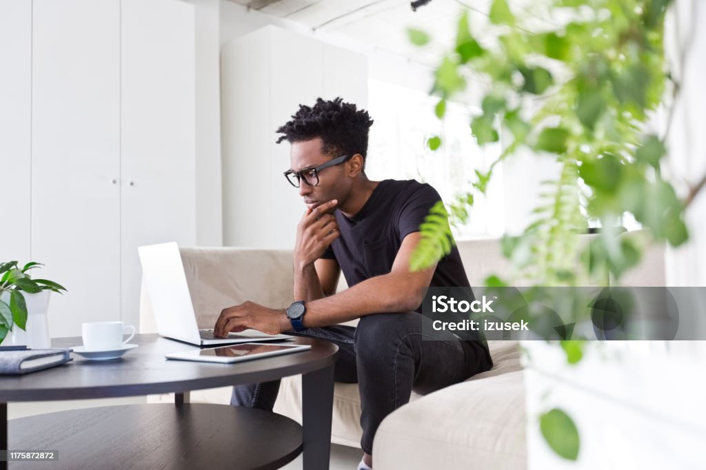 Confident male executive working on sofa in office Confident male executive using laptop while sitting on sofa at workplace. Afro hipster professional is working at creative office. He is in smart casual. 30-34 Years Stock Photo