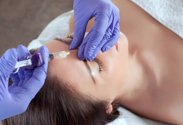 il ya une femme et un cosmétologue, la femme est couchée et le médecin fait la procédure d'injections faciales pour le resserrement et le lissage des rides dans un salon de beauté. soins de la peau cosmétologie. - mesotherapy photos et images de collection