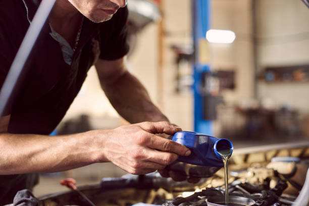 istock Engine oil changing in auto workshop. Focus on pouring grease from bottle by repairman hands. Maintenance car engine 1175875353