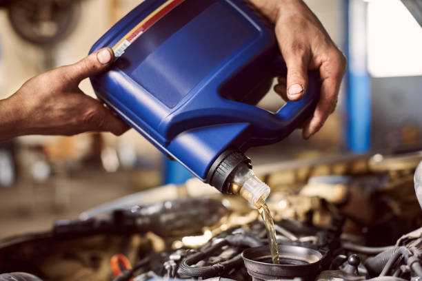 istock Macro view of blue bottle in dirty hands pouring oil into car engine. Replacing engine lubricants in auto service center 1175875363