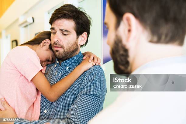 Doctor Looking At Father With Ill Girl In Hospital Stock Photo - Download Image Now - Child, Doctor, Sadness