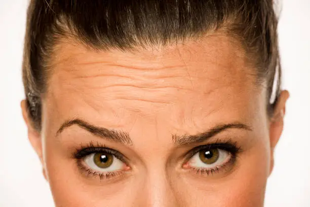 young woman showing her forehead wrinkles with her fingers on a white background