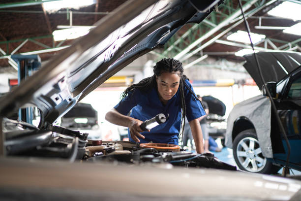Woman repairing a car in auto repair shop Woman repairing a car in auto repair shop adjusting stock pictures, royalty-free photos & images