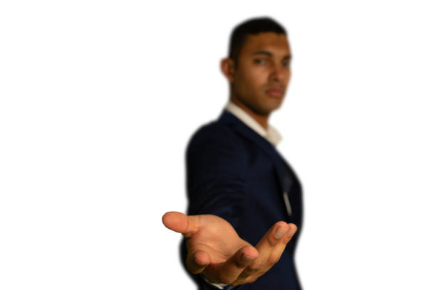 Front view close up of a young mixed race businessman wearing black jacket and white shirt, with arm raised and hand held out to camera, palm up, to hold or receive, focus on the foreground