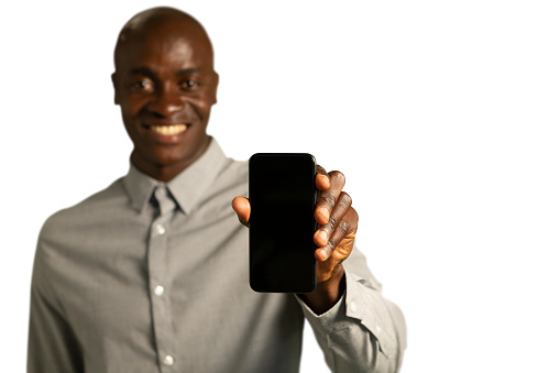 Front view close up of a smiling young African American man holding out his smartphone and showing the screen to camera, focus on the foreground