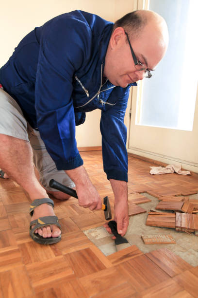 istock Construction worker and constructor is working on renovation of apartment. Handyman is removing old wooden parquet flooring using yellow hammer and scraping tool. Builder dismantles parquet floor. 1175896746