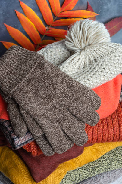 istock Stack of folded warm knitted women's sweaters, scarf, hat with pompom, gloves in warm colors and autumn leaves. Closeup 1175898677