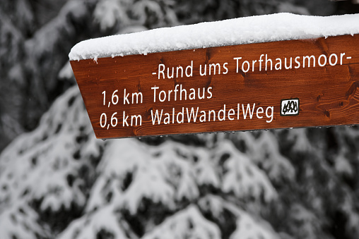 Close-up photo of snow covered wooden directional signpost with labeling \