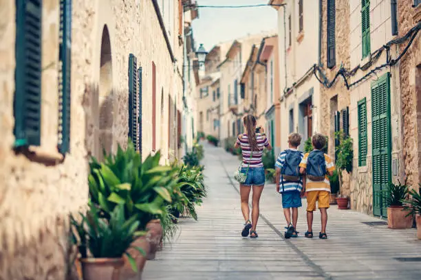 Kids tourists walking beautiful street of a mediterranean town. Sunny summer day. Alcudia, Mallorca, Spain.