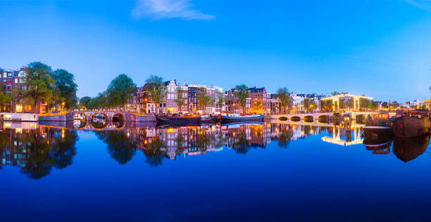 vue panoramique du pont magere brug et des maisons latérales de canal sur la rivière amstel à twilight, amsterdam, pays-bas - magere brug photos et images de collection