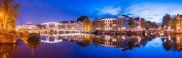 vue panoramique du pont magere brug et des maisons latérales de canal sur la rivière amstel à twilight, amsterdam, pays-bas - magere brug photos et images de collection