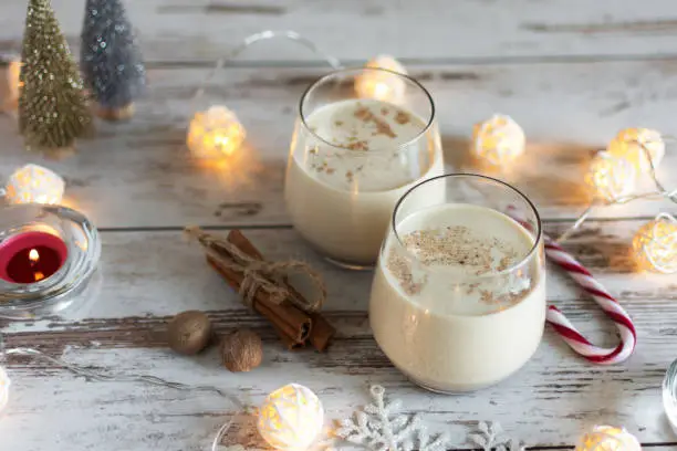 Fresh eggnog with cinnamon and nutmeg for christmas holiday with christmas decorations on wooden background..