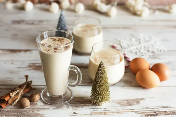 Fresh eggnog with cinnamon and nutmeg for christmas holiday with christmas decorations on wooden background..