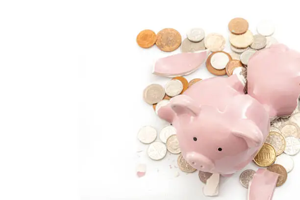 Break the bank, economic downturn and bankruptcy concept theme with a broken piggy bank and scattered coins isolated on white background with copy space