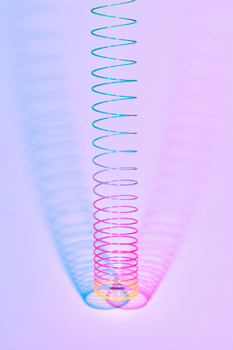 Hunging multicolored plastic spiral toy with two duotone shadows on a pastel pink background, copy space.