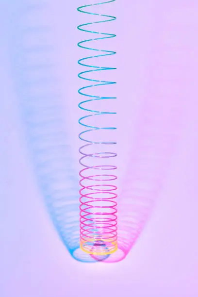 Hunging multicolored plastic spiral toy with two duotone shadows on a pastel pink background, copy space.