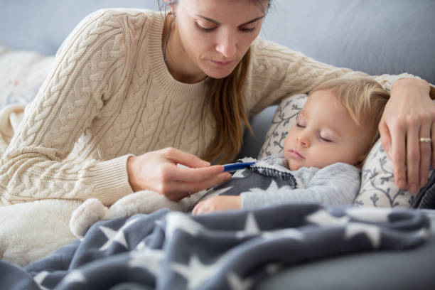 Sick child, toddler boy lying in bed with a fever, resting at home Sick child, toddler boy lying on the couch in living room with a fever, mom cheching his temperature, resting at home plush bear stock pictures, royalty-free photos & images