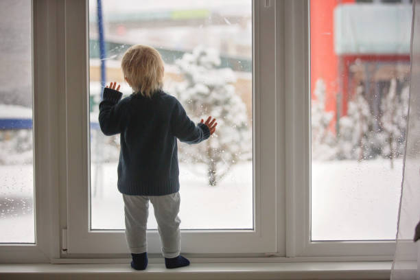 małe dziecko stojące przed dużymi francuskimi drzwiami, opierające się o to, patrząc na zewnątrz na śnieżną naturę - blizzard house storm snow zdjęcia i obrazy z banku zdjęć