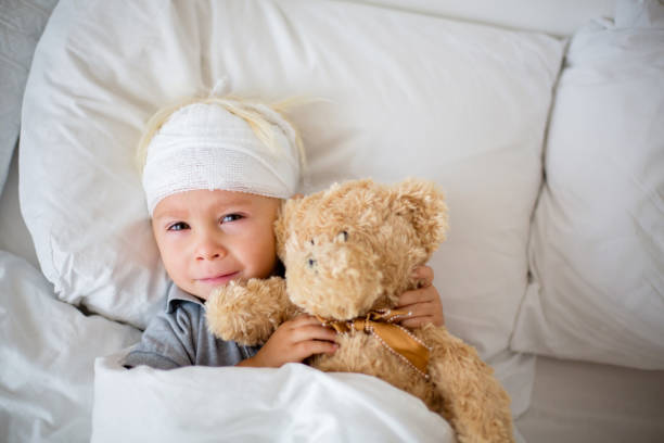 niño pequeño con lesión en la cabeza, acostado en la cama, cansado - child physical injury teddy bear wound fotografías e imágenes de stock