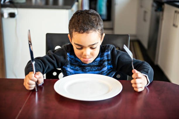 menino que senta-se na tabela da cozinha com placa vazia - healthy eating snack child domestic kitchen - fotografias e filmes do acervo