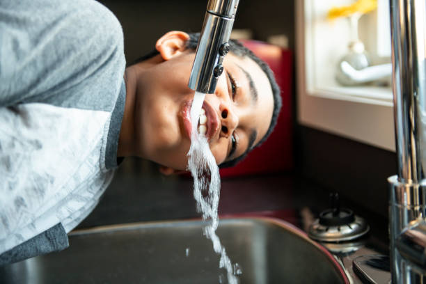 子供のアフロアメリカ人の男の子は、彼の口に水を取り、台所で飲みます。 - cleaning environment clean earth ストックフォトと画像