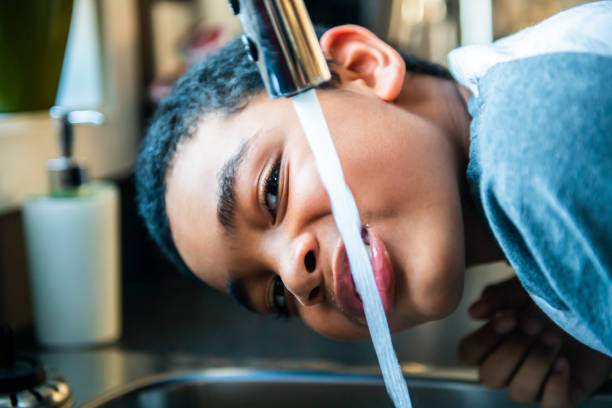 子供のアフロアメリカ人の男の子は、彼の口に水を取り、台所で飲みます。 - cleaning environment clean earth ストックフォトと画像