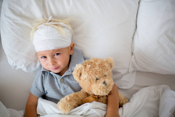 niño pequeño con lesión en la cabeza, acostado en la cama, cansado - child physical injury teddy bear wound fotografías e imágenes de stock