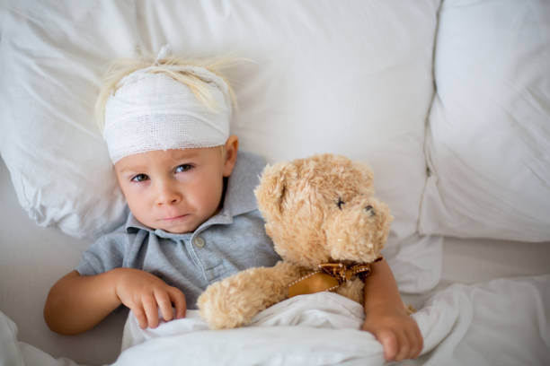 niño pequeño con lesión en la cabeza, acostado en la cama, cansado - child physical injury teddy bear wound fotografías e imágenes de stock