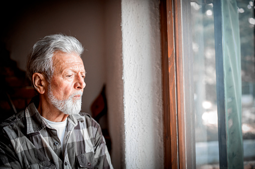 Sad Mature man Suffering From Agoraphobia Looking Out Of Window