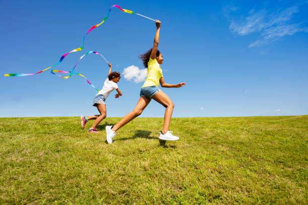 istock Girls run with ribbon over grass, sky background 1175916531