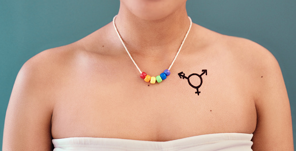 Studio shot of an unrecognizable woman posing with an LGBTQ symbol drawn on her chest while wearing a rainbow necklace