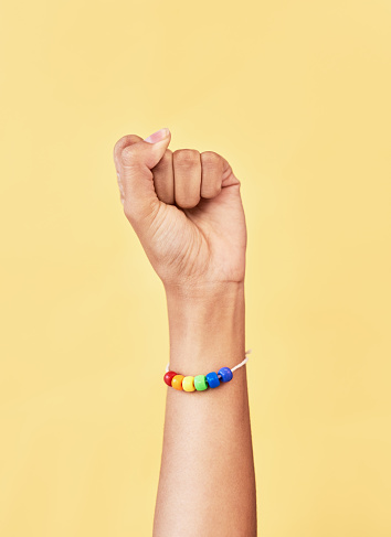 Studio shot of an unrecognizable woman raising a fist while wearing a rainbow bracelet