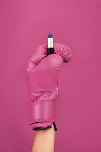 Studio shot of an unrecognizable sportswoman holding a lipstick while wearing a boxing glove against a purple background