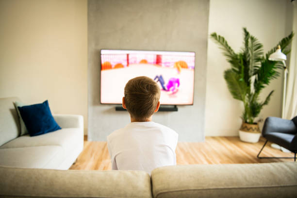 istock Back view image of cute boy sitting on sofa and watching TV. 1175920820