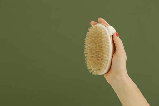 Woman holding the wooden brush for dry brushing procedure. Dry brushing is a procedure to reduce cellulite, detoxify the lymphatic system, and achieve beautifully smooth skin.