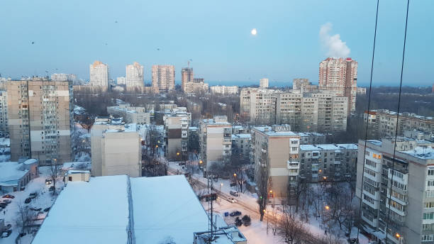 istock Blurry white moon in blue dusky sky. Retro high-rise buildings with rooftops covered by clean snow blue colored in evening light. Aerial view to Odessa of Ukraine in Europe. Shiny city lights. 1175930973