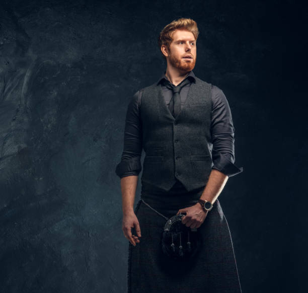 istock Redhead man dressed in an elegant vest with tie and kilt in studio against a dark textured wall 1175932292