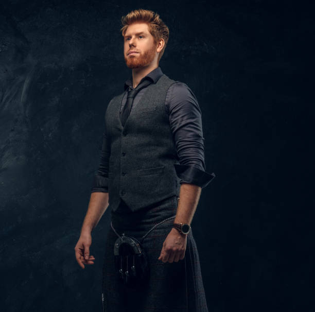 istock Redhead man dressed in an elegant vest with tie and kilt in studio against a dark textured wall 1175932746