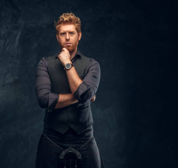 istock Redhead man dressed in an elegant vest with tie and kilt posing with thoughtful look in studio against a dark textured wall 1175932814