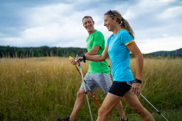 active smiling middle aged couple doing nordic walking sport in grassland with  shallow focus cloudy overcast sky dark clouds side view