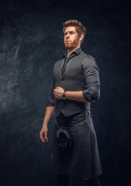 istock Redhead man dressed in an elegant vest with tie and kilt in studio against a dark textured wall 1175932941