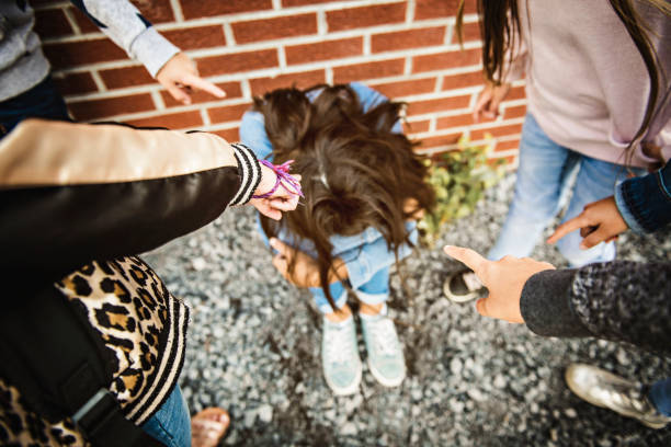 triste momento di intimidazione. ragazza sedersi a terra bullismo in schoolyard - bullying sneering rejection child foto e immagini stock