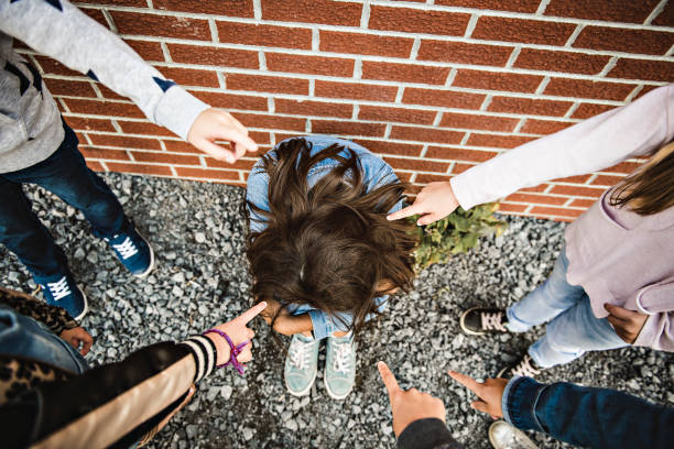 smutny moment zastraszania. dziewczyna siedzieć na ziemi zastraszanie w schoolyard - bullying sneering rejection child zdjęcia i obrazy z banku zdjęć