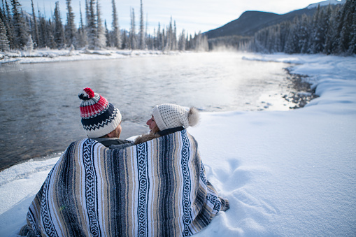 Two people relaxing in winter by the river contemplating nature under a blanket